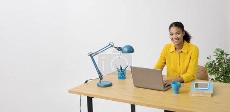 Téléchargez les photos : Jeune femme assise à son bureau et tapant sur un ordinateur portable, espace de copie - en image libre de droit