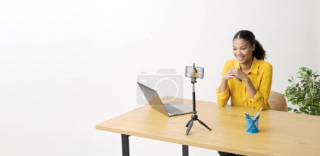 Photo for Young confident youtuber sitting at her desk and recording a video for social media using a smartphone - Royalty Free Image