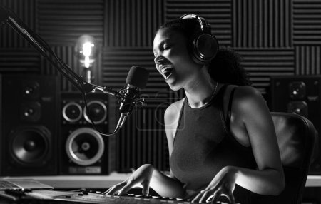 Téléchargez les photos : Jeune artiste féminine enregistrant une chanson en studio, elle chante et joue du clavier - en image libre de droit