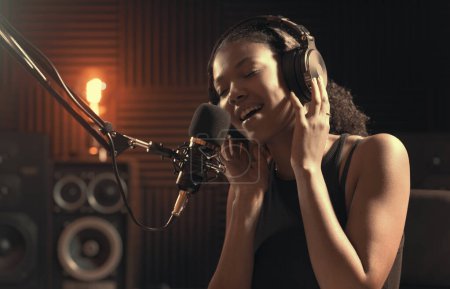 Foto de Una joven atractiva que trabaja en el estudio de grabación, está cantando en un micrófono - Imagen libre de derechos