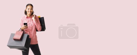 Photo for Happy young woman doing shopping on Black Friday, she is holding her smartphone and many shopping bags - Royalty Free Image