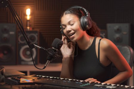 Téléchargez les photos : Belle jeune femme dans le studio d'enregistrement, elle chante et joue du clavier - en image libre de droit