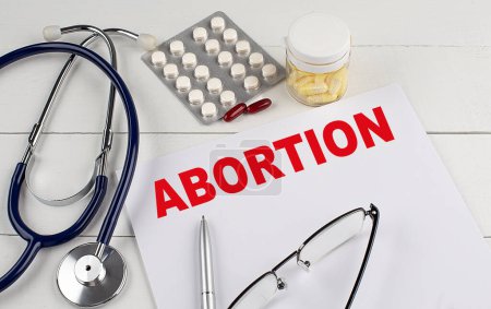 Téléchargez les photos : ABORTION mot sur un papier avec stéthoscope et pilules - en image libre de droit