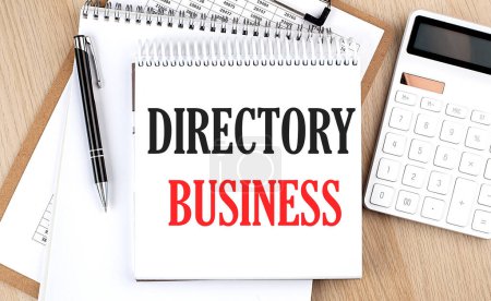 DIRECTORY BUSINESS está escrito en bloc de notas blanco cerca de una calculadora, portapapeles y bolígrafo. Negocio
