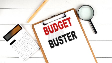 Photo for BUDGET BUSTER words on clipboard, with calculator, magnifier and pencil on white wooden background - Royalty Free Image
