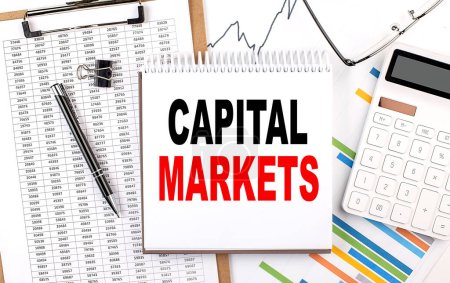 Photo for CAPITAL MARKETS text on a notebook with chart, calculator and pen - Royalty Free Image