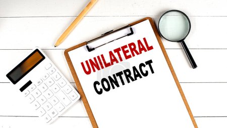 Foto de UNILATERAL CONTRACT words on clipboard, with calculator, magnifier and pencil on white wooden background - Imagen libre de derechos