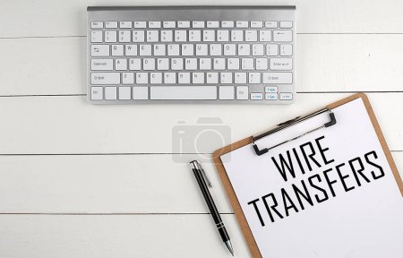 Téléchargez les photos : Home office workspace with keyboard, clipboard and pen with text WIRE TRANSFERS on a white wooden background ,business concept - en image libre de droit