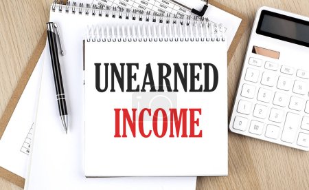 Photo for UNEARNED INCOME is written in white notepad near a calculator, clipboard and pen. Business - Royalty Free Image