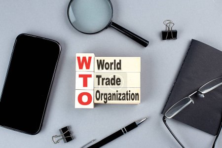 Foto de Cubos de madera OMC - Organización Mundial del Comercio wtih notebook, lupa y smartphone, business - Imagen libre de derechos