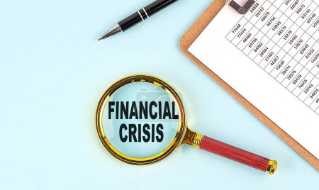 Téléchargez les photos : FINANCIAL CRISIS text on a magnifier with clipboard on blue background - en image libre de droit