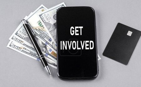 Foto de Tarjeta de crédito y texto INVOLÚCRATE en un smartphone con dólares y bolígrafo. Concepto empresarial - Imagen libre de derechos