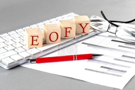 EOFY geschrieben auf Holzwürfel auf der Tastatur mit Diagramm auf grauem Hintergrund