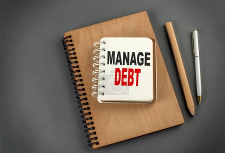 MANAGE DEBT text on a notebook with pen and pencil on grey background