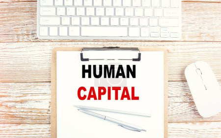 Photo for HUMAN CAPITAL text on clipboard with keyboard on wooden background - Royalty Free Image