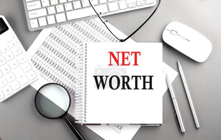 NET WORTH text on a notepad on chart with keyboard and calculator on grey background
