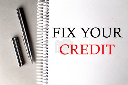 FIX YOUR CREDIT text on notebook with pen on grey background