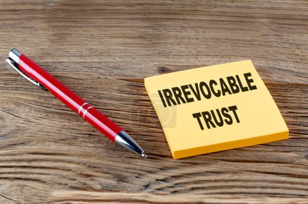 IRREVOCABLE TRUST text on a sticky with pen on the wooden background