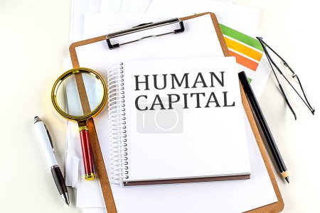 Photo for HUMAN CAPITAL text on a notebook with clipboard on white background - Royalty Free Image