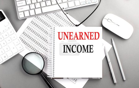 Photo for UNEARNED INCOME text on a notepad on chart with keyboard and calculator on grey background - Royalty Free Image