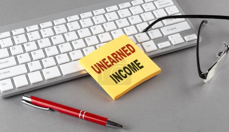 Photo for UNEARNED INCOME text on sticky with keyboard, pen glasses on grey background - Royalty Free Image