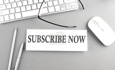 SUBSCRIBE NOW text on a paper with keyboard on grey background