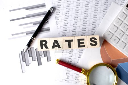 RATES text on a wooden block on graph background with pen and magnifier