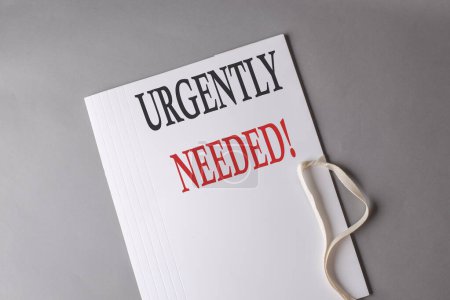 Photo for URGENTLY NEEDED text on a white folder on grey background - Royalty Free Image