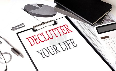 Photo for DECLUTTER YOUR LIFE text on a paper clipboard with chart and notebook on withe background - Royalty Free Image