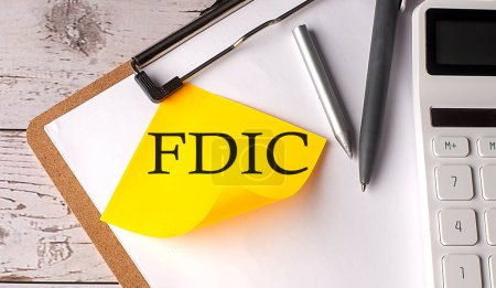 Photo for FDIC word on yellow sticky with calculator, pen and clipboard - Royalty Free Image