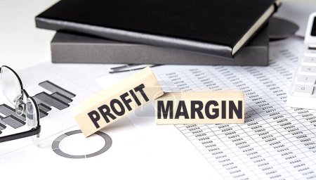 PROFIT MARGIN - text on wooden block with chart and notebook