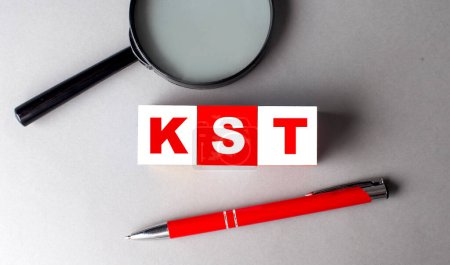 Téléchargez les photos : Mot KST sur un cube en bois avec stylo et loupe - en image libre de droit