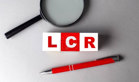 Téléchargez les photos : LCR- LIQUIDITY COVERAGE RATIO mot sur un cube en bois avec stylo et loupe - en image libre de droit