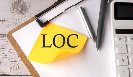 Foto de Palabra LOC en amarillo pegajoso con calculadora, pluma y portapapeles - Imagen libre de derechos