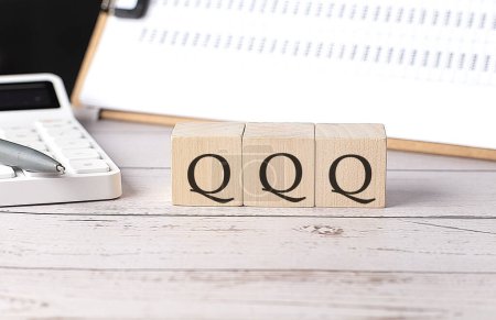 QQQ-Wort auf Holzblock mit Klemmbrett und Taschenrechner