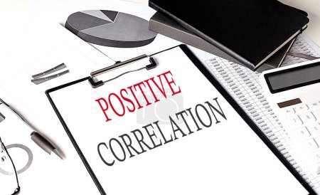 Photo for POSITIVE CORRELATION text on a paper clipboard with chart and notebook on withe background - Royalty Free Image