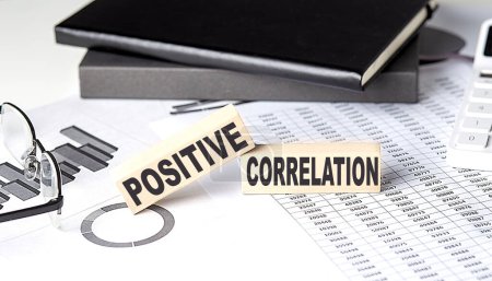 Photo for POSITIVE CORRELATION - text on wooden block with chart and notebook - Royalty Free Image