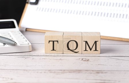 TQM word on wooden block with clipboard and calculator