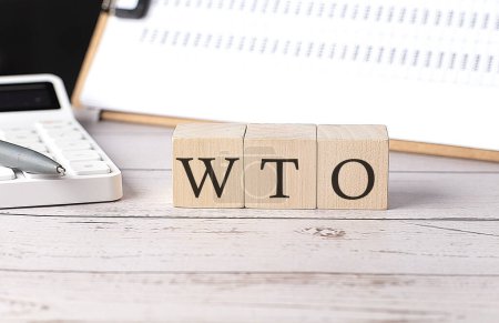 Foto de OMC - Palabra de la Organización Mundial del Comercio sobre un bloque de madera con portapapeles y calculadora - Imagen libre de derechos