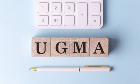Foto de UGMA en cubos de madera con pluma y calculadora, concepto financiero - Imagen libre de derechos