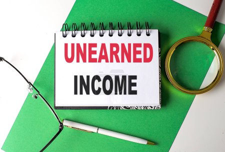 Photo for UNEARNED INCOME text on a notebook on green paper - Royalty Free Image