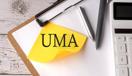 Foto de Palabra UMA en amarillo pegajoso con calculadora, pluma y portapapeles - Imagen libre de derechos