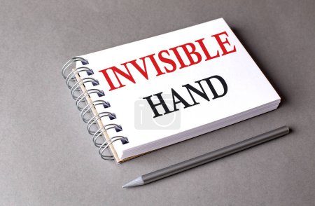 INVISIBLE HAND word on a notebook on grey background