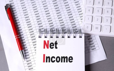 NET INCOME text on a notebook with pen, calculator and chart on grey background