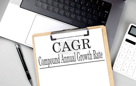 Photo for Paper clipboard with CAGR compound annual growth rate on a laptop with pen and calculator - Royalty Free Image