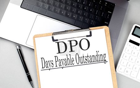Paper clipboard with DPO Days Payable Outstanding on a laptop with pen and calculator