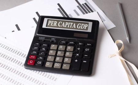 Téléchargez les photos : Texte du PIB par habitant sur une calculatrice avec graphique sur fond gris - en image libre de droit