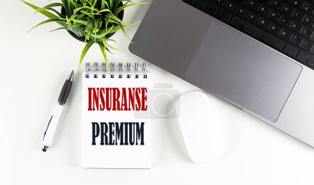 INSURANCE PREMIUM text written on a notebook with laptop and mouse , white background