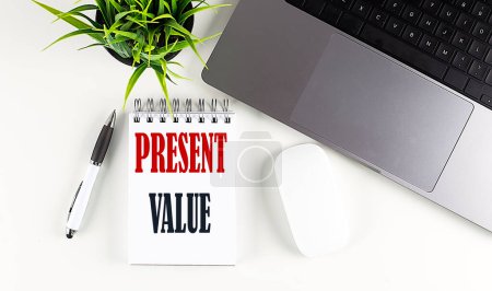 PRESENT VALUE text written on a notebook with laptop and mouse , white background