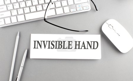 INVISIBLE HAND text on a paper with keyboard on grey background